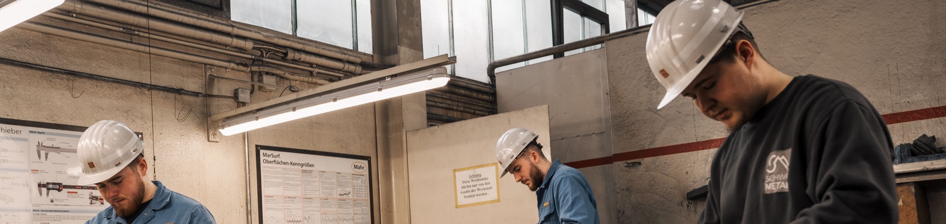 Drei Azubis mit Schutzhelmen arbeiten in einer Werkstatt