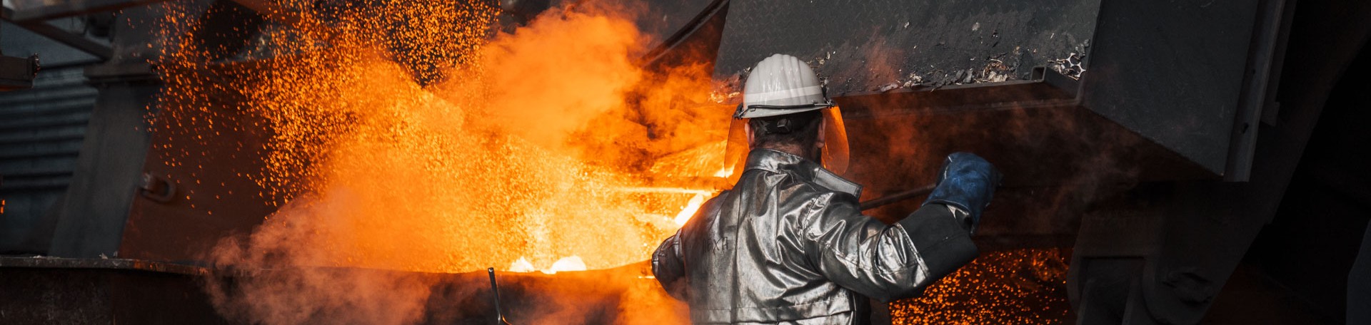 Arbeiter in Schutzkleidung überwacht glühendes, flüssiges Metall am Hochofen.